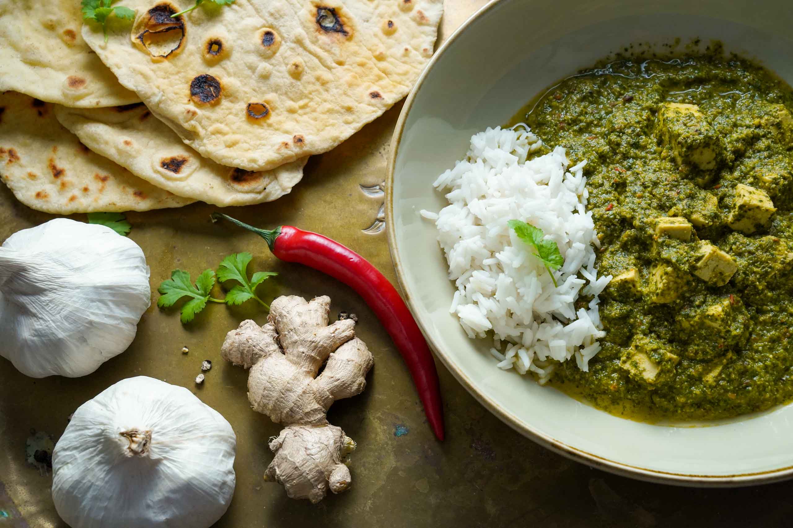 egane Palak Paneer in zwei Schüsseln, dazu Naanbrot. Dekoriert mit frischen Zutaten wie Chili und Knoblauch. Detailansicht.