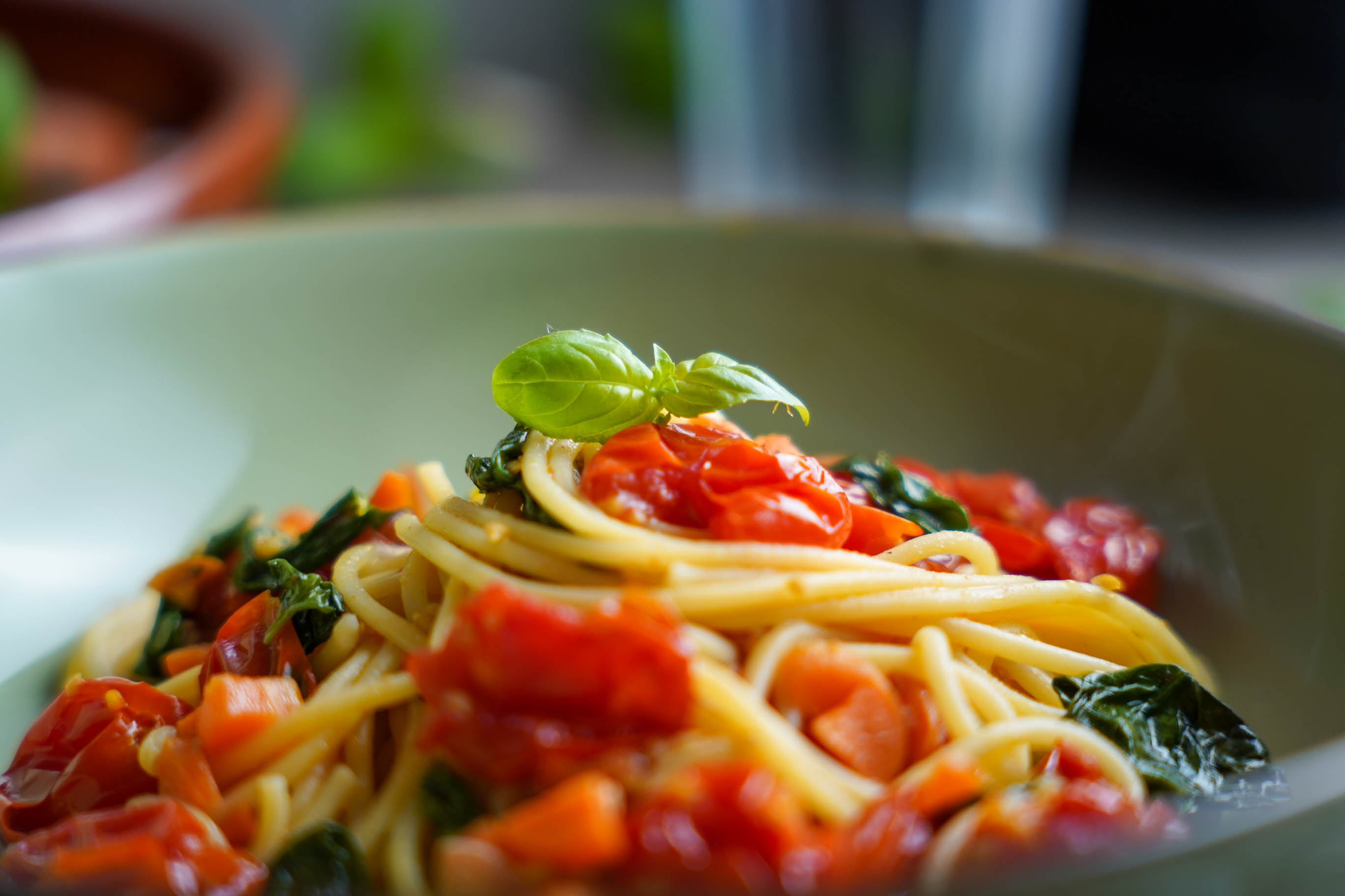 Veganes Spaghetti Pomodoro in einem Teller angerichtet. Fokus auf ein Basilikumblatt, welches auf den Nudeln trohnt.